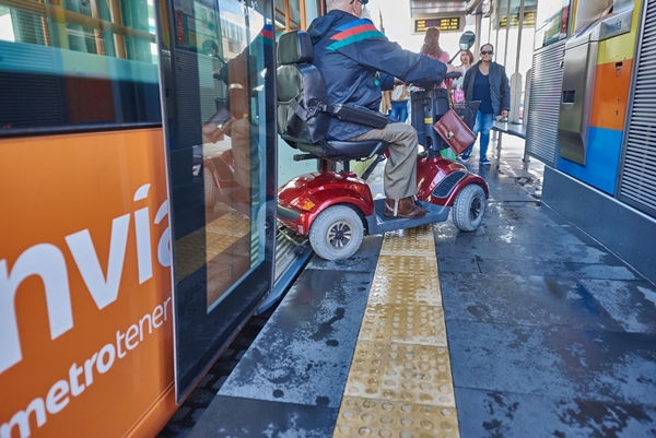 Usuario en silla de ruedas eléctrica sale del tranvía a la parada. 